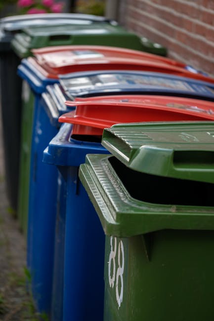 A person's arm extending from the left side of the frame holds a tied closed green and blue plastic rubbish bag, which appears to contain waste. The bag is slightly transparent, revealing some indisti